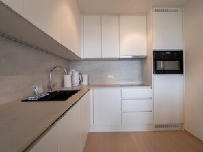 A modern kitchen with white cabinetry, a stainless steel sink, and a built-in oven. - Astrid with parking & airco by Interhome (Bredene)