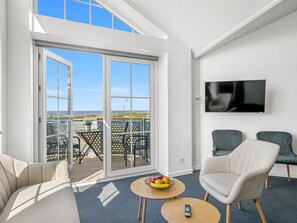 A modern living room with a large sliding glass door leading to a balcony, a flat-screen TV mounted on the wall, and two upholstered chairs. - "Zuhra" - 50m to the fjord by Interhome (Tarm)