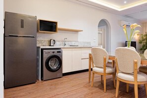A compact kitchen with a refrigerator, microwave, and washing machine. There are wooden chairs and a table with a vase of flowers. - Vesta - New Cairo Residence  (new cairo)