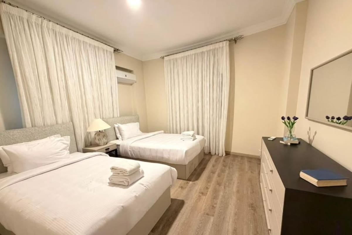 A hotel room with two beds, a desk, a mirror, and a window with curtains.