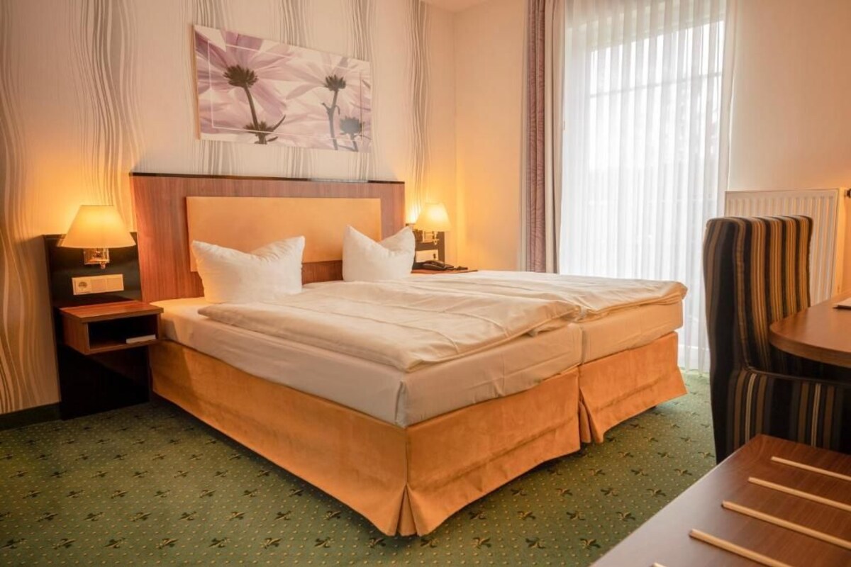 A hotel room with a large bed, two bedside tables with lamps, a chair, and a painting on the wall.