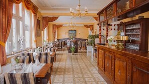 A restaurant with a long counter, multiple tables, and chairs. There is a bar area with shelves of glasses and bottles. - Alte Landratsvilla Hotel Bender GmbH  (Westerburg)