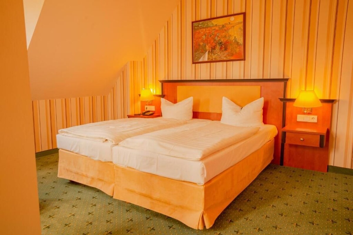 A double bed with two nightstands, each with a lamp, in a room with striped wallpaper and a painting above the bed.
