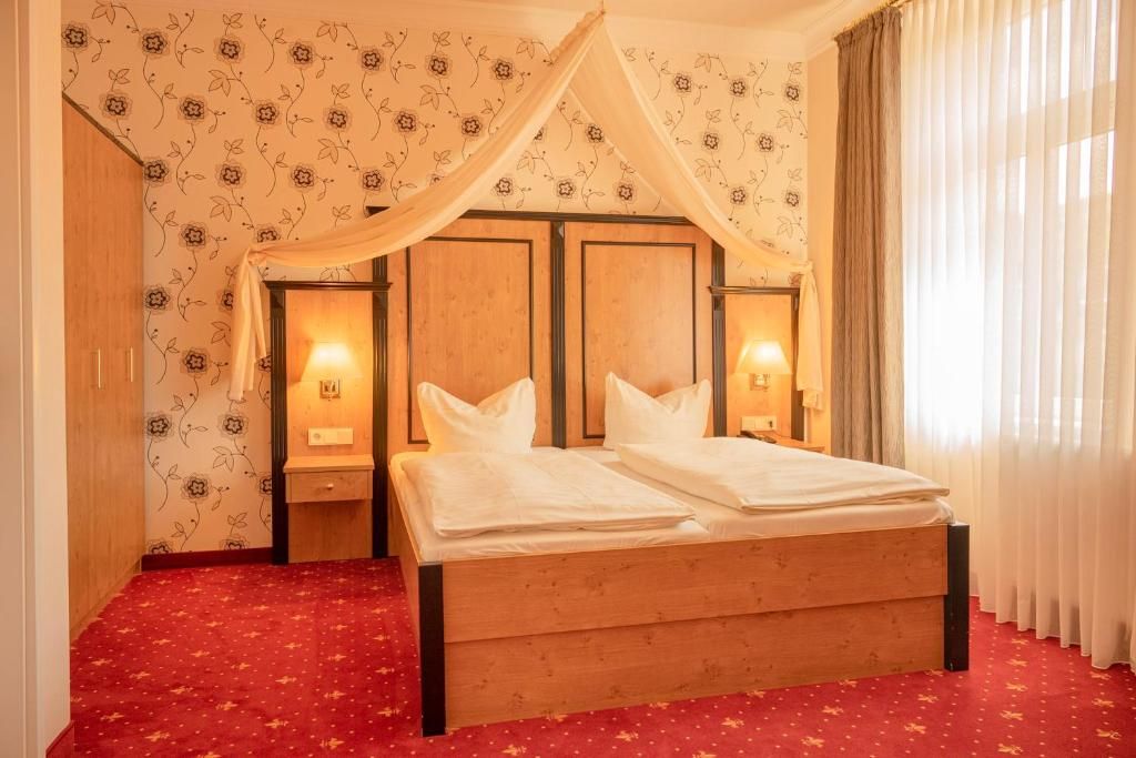Ein Hotelzimmer mit einem hölzernen Bett, blumigem Wandpapier und einem roten Teppich.