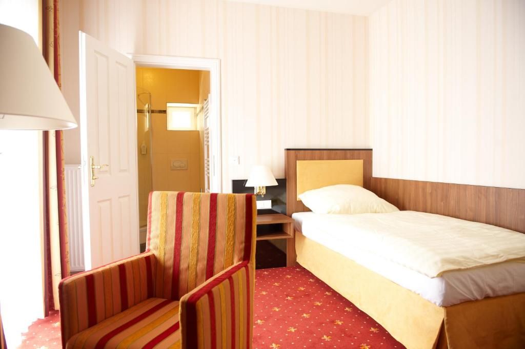 Una habitación de hotel con cama, una silla, una mesita de noche y una puerta que da a un baño.