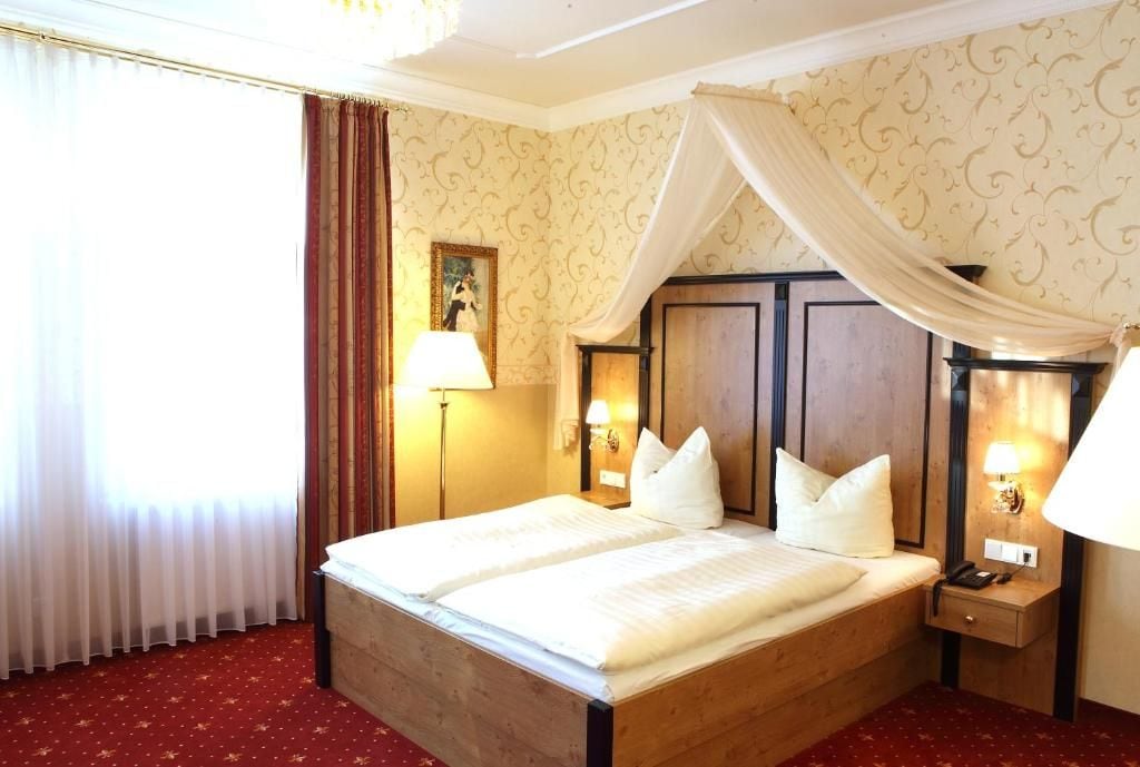 A hotel room with a large bed, a nightstand with a lamp, a wooden headboard, and a picture on the wall.