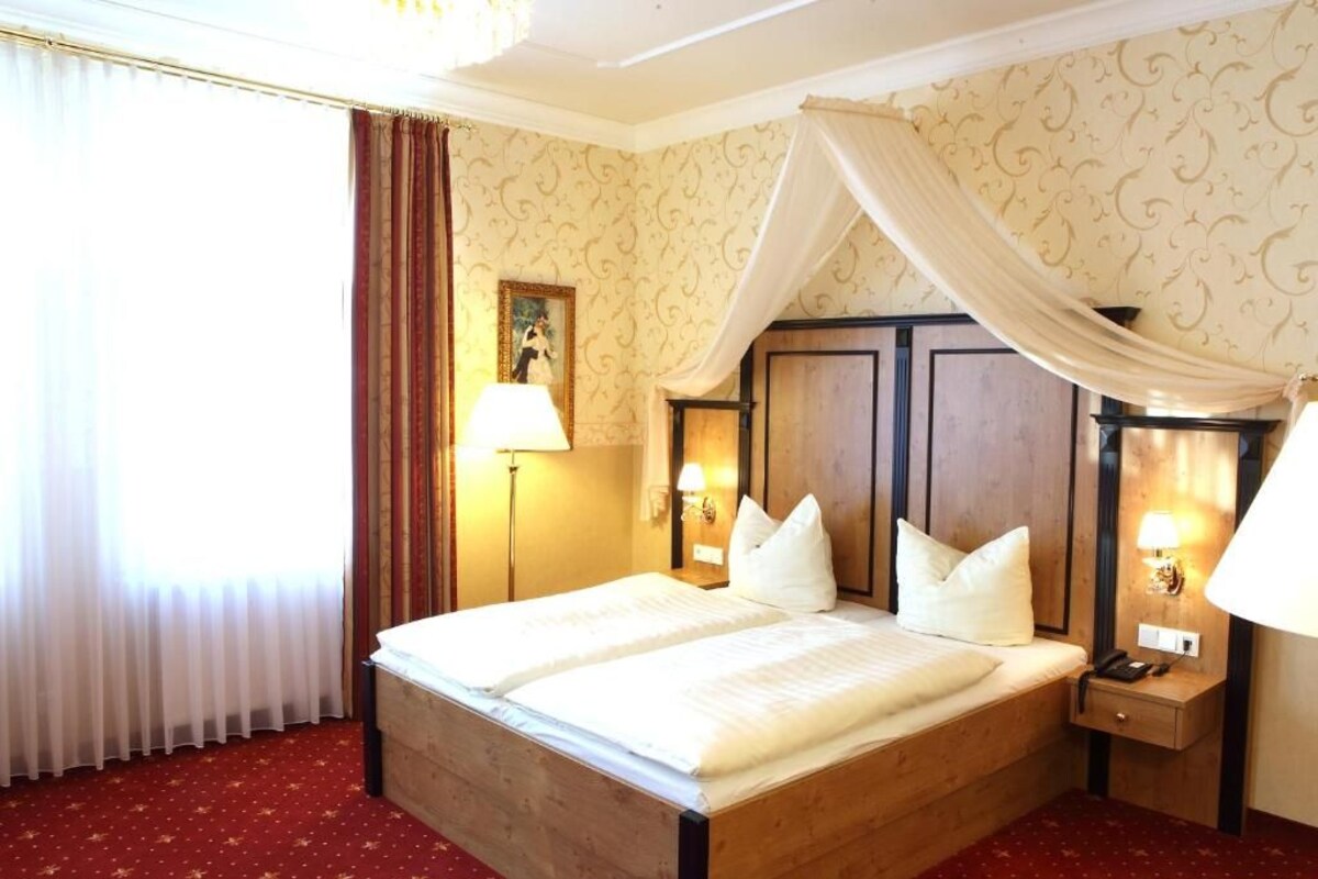 A hotel room with a large bed, a nightstand with a lamp, a wooden headboard, and a picture on the wall.