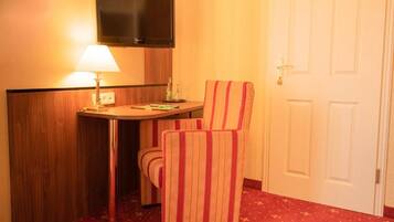 Una habitación de hotel con una cama individual, una mesita de noche con lámpara, un televisor montado en la pared y un sillón a rayas.