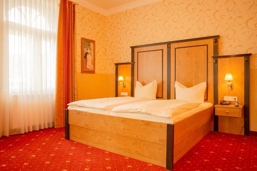 Una habitación de hotel con una cama de madera, dos lámparas de noche, una alfombra roja y un cuadro en la pared.