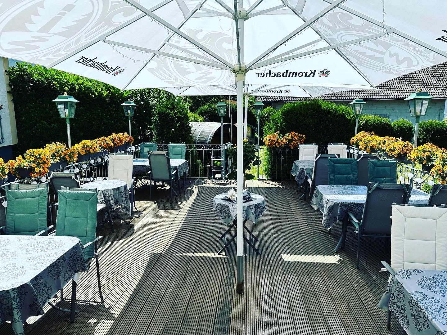 Un área de comedor al aire libre con mesas y sillas, cubierta por una sombrilla grande, rodeada de vegetación.