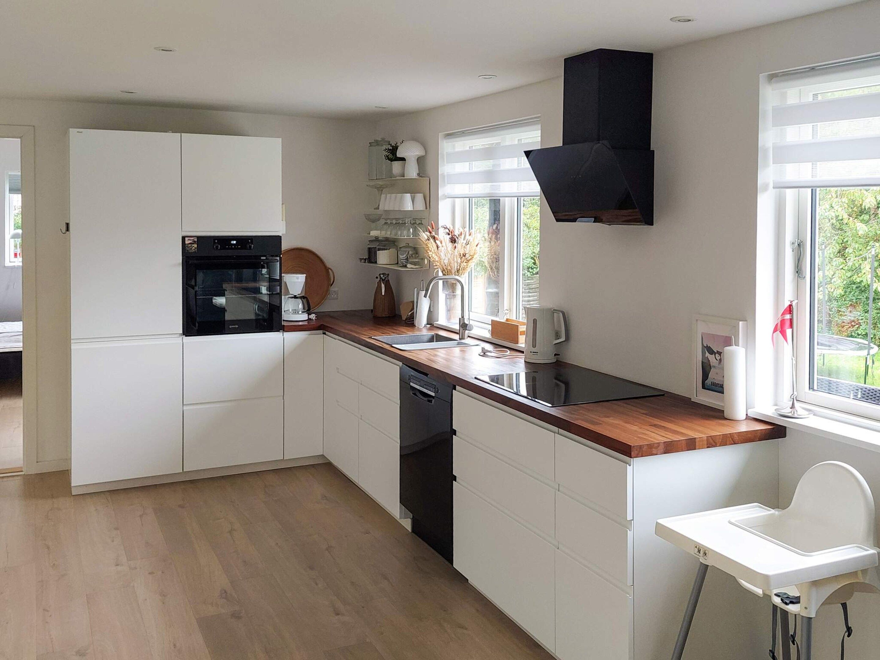 A modern kitchen with white cabinetry, a built-in oven, and a black range hood.