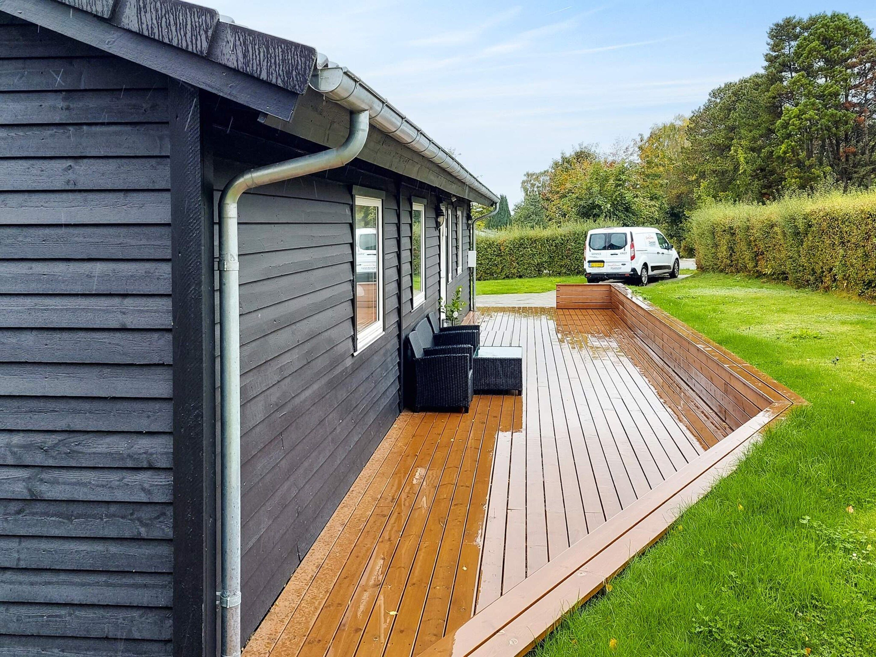 A wooden deck adjacent to a building with a metal gutter system.