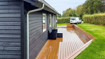 A wooden deck adjacent to a building with a metal gutter system.