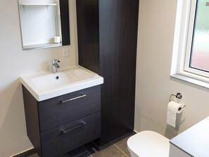A modern bathroom with a white sink, dark cabinetry, a mirror, and a toilet. - 6 Person Holiday Home in Melby (Melby)