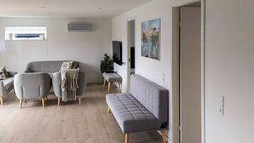 A modern living room with a grey sofa, two armchairs, a bench, and a flat-screen TV mounted on the wall.