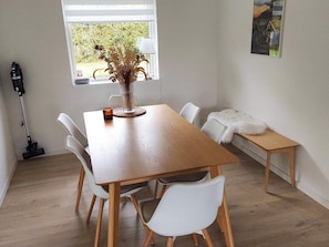 A dining area with a wooden table, white chairs, a vase with dried plants, a lamp, and a window with a view of greenery. - 6 Person Holiday Home in Melby (Melby)