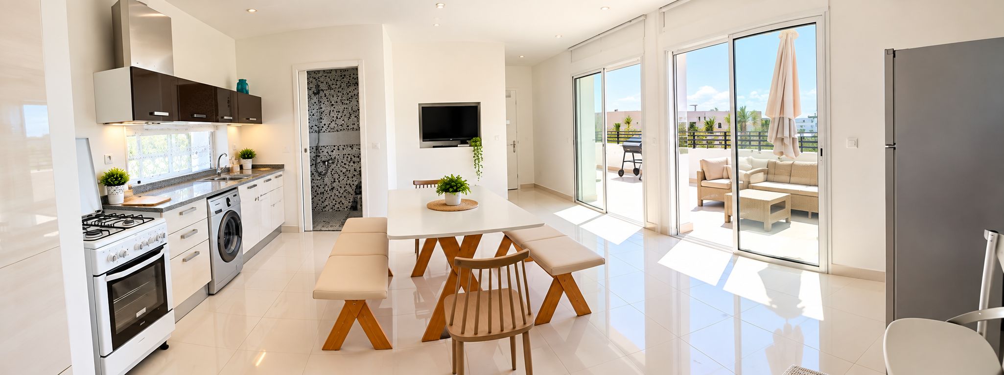 A modern kitchen with a dining area, a TV, and a sliding glass door leading to an outdoor seating area.