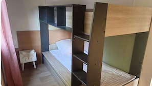 Una cama individual con dos literas, cabecera de madera y una mesita de noche con un adorno de gato.