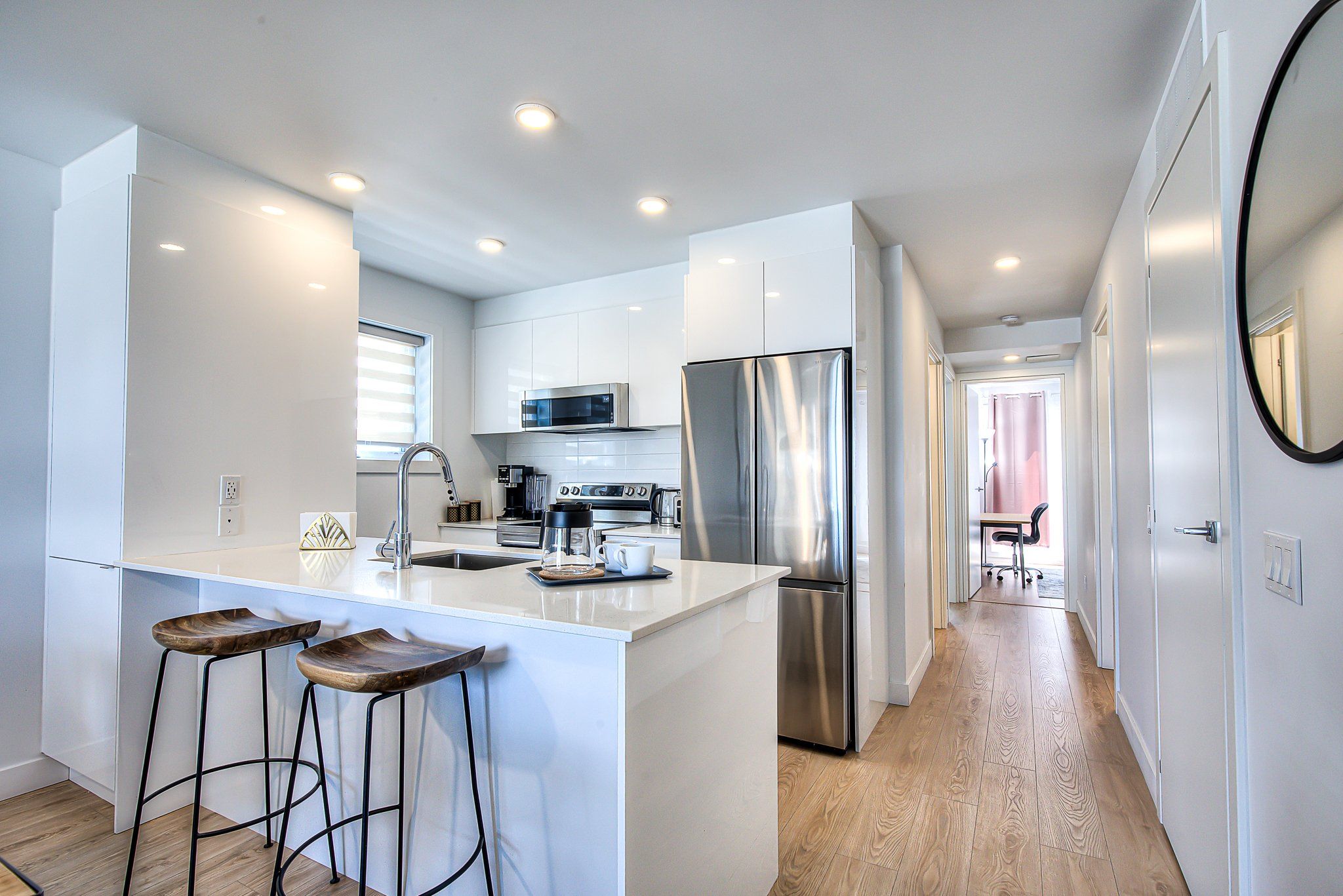 A modern kitchen with white cabinetry, stainless steel appliances, and a central island with bar stools.