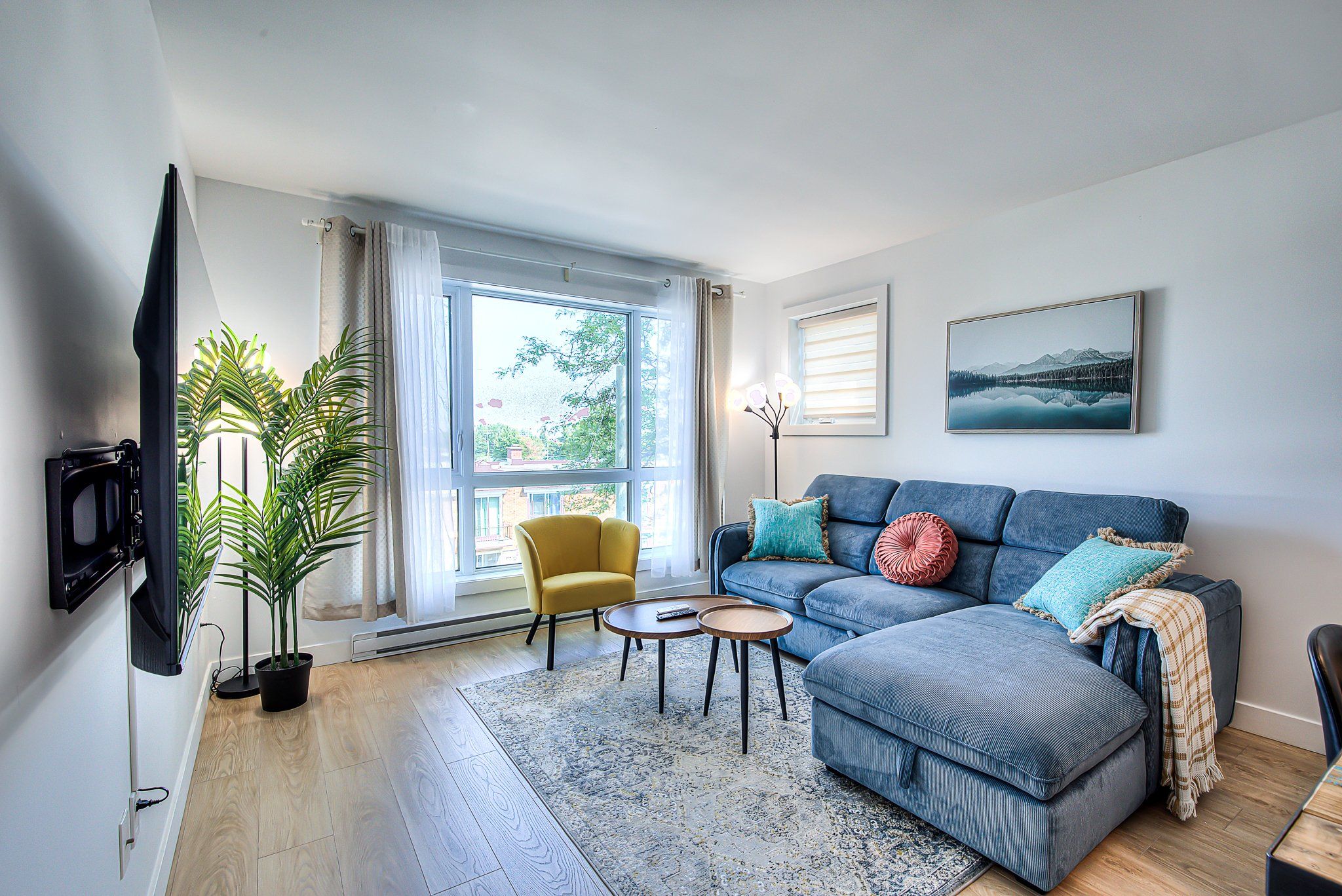A living room with a sofa, a yellow armchair, a coffee table, a potted plant, and a television.