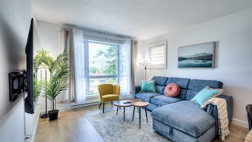 A living room with a sofa, a yellow armchair, a coffee table, a potted plant, and a television.