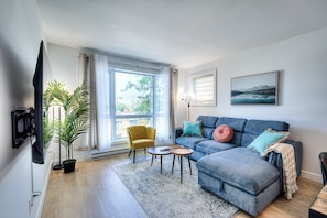 A living room with a sofa, a yellow armchair, a coffee table, a potted plant, and a television. - Elegant 3BR Condo for Families | 2 Baths, AC & Fast WiFi (Montréal)