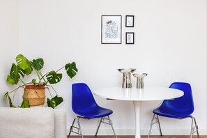 A room with a white round table, two blue chairs, a potted plant, and two framed pictures on the wall. - Modern 2-Bed Flat in Highbury • Victoria Line (London)