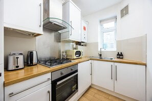 A modern kitchen with a gas stove, toaster, microwave, and a window. - Modern 2-Bed Flat in Highbury • Victoria Line (London)