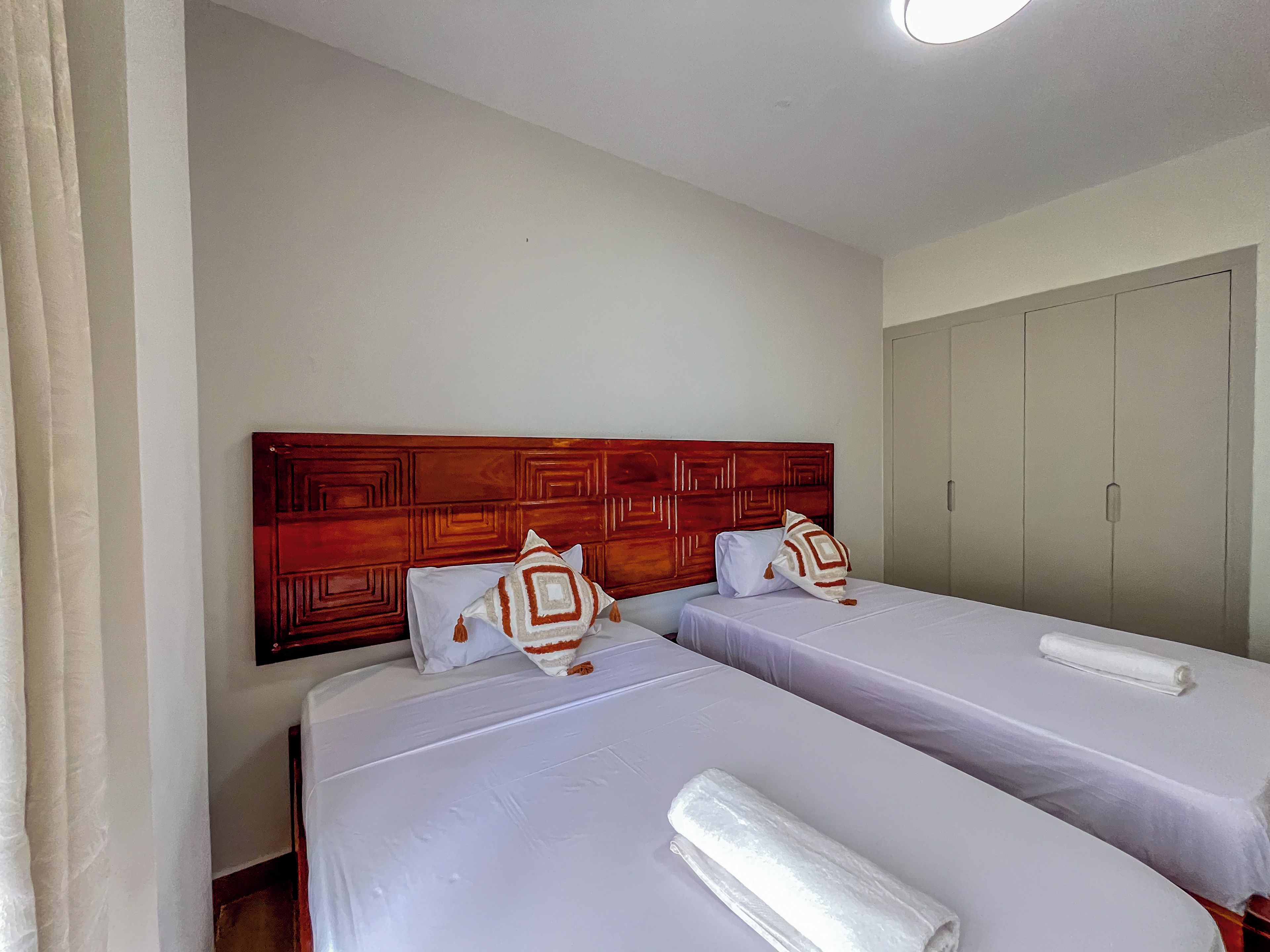 A hotel room with two beds, a wooden headboard, and a wardrobe.
