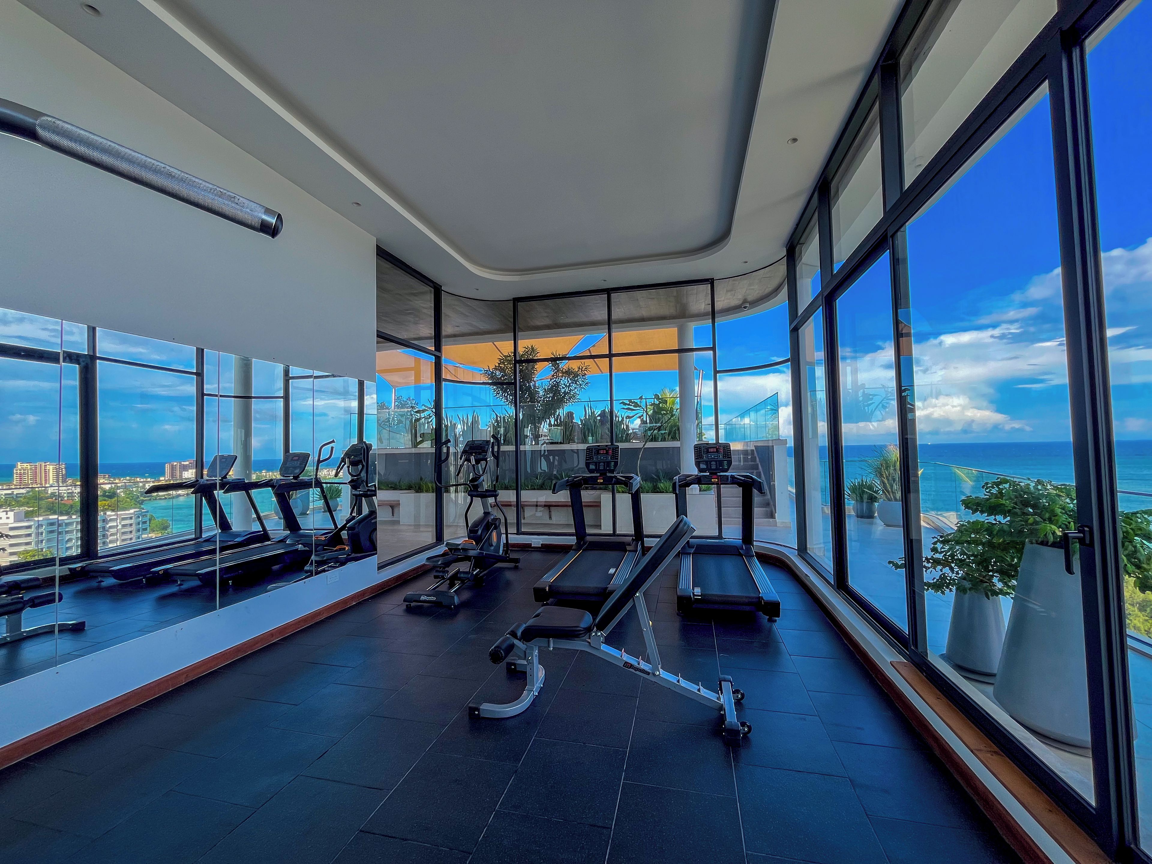 Een moderne sportschool met trainingsapparatuur en grote ramen met uitzicht op zee.