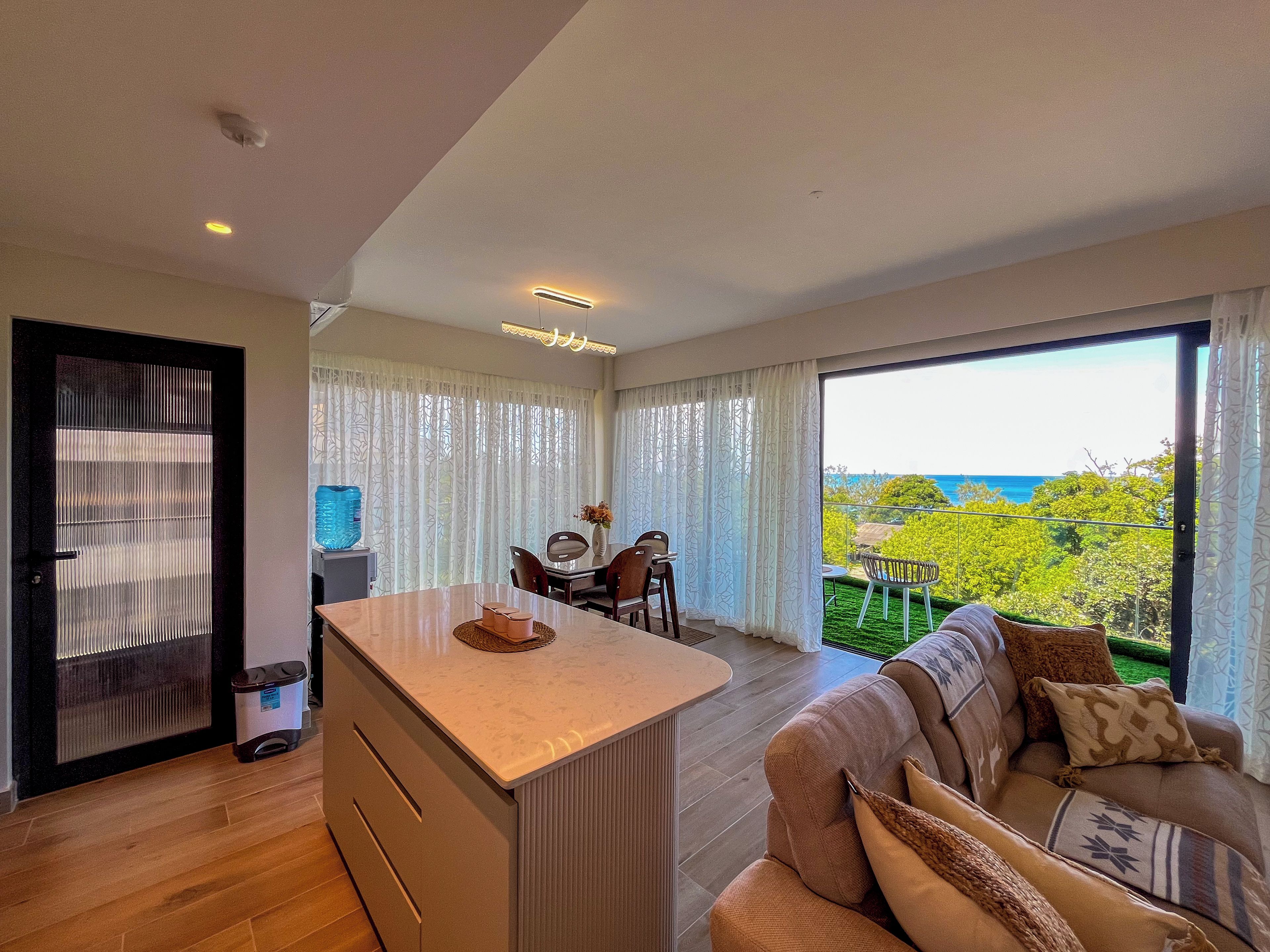 A modern interior with a dining area, a sofa, and a view of the outdoors.