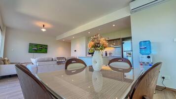 A modern living room with a glass dining table, a sofa, and a kitchen area in the background.
