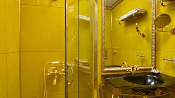 A bathroom with a glass shower enclosure, a sink with a gold faucet, and a mirror with a gold frame.