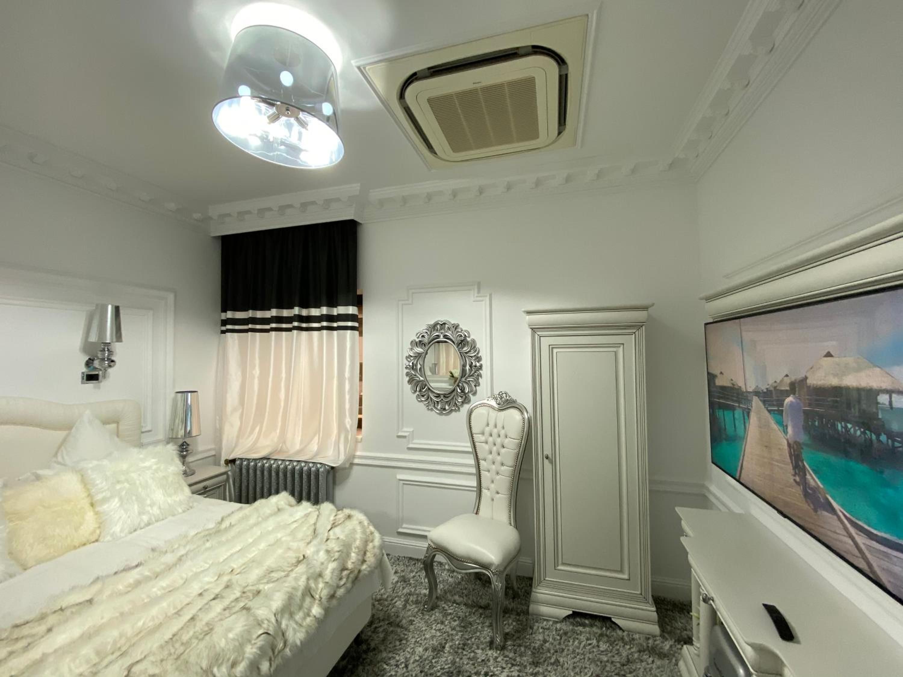 A hotel room with a bed, a chair, a wardrobe, a mirror, a radiator, and a television.