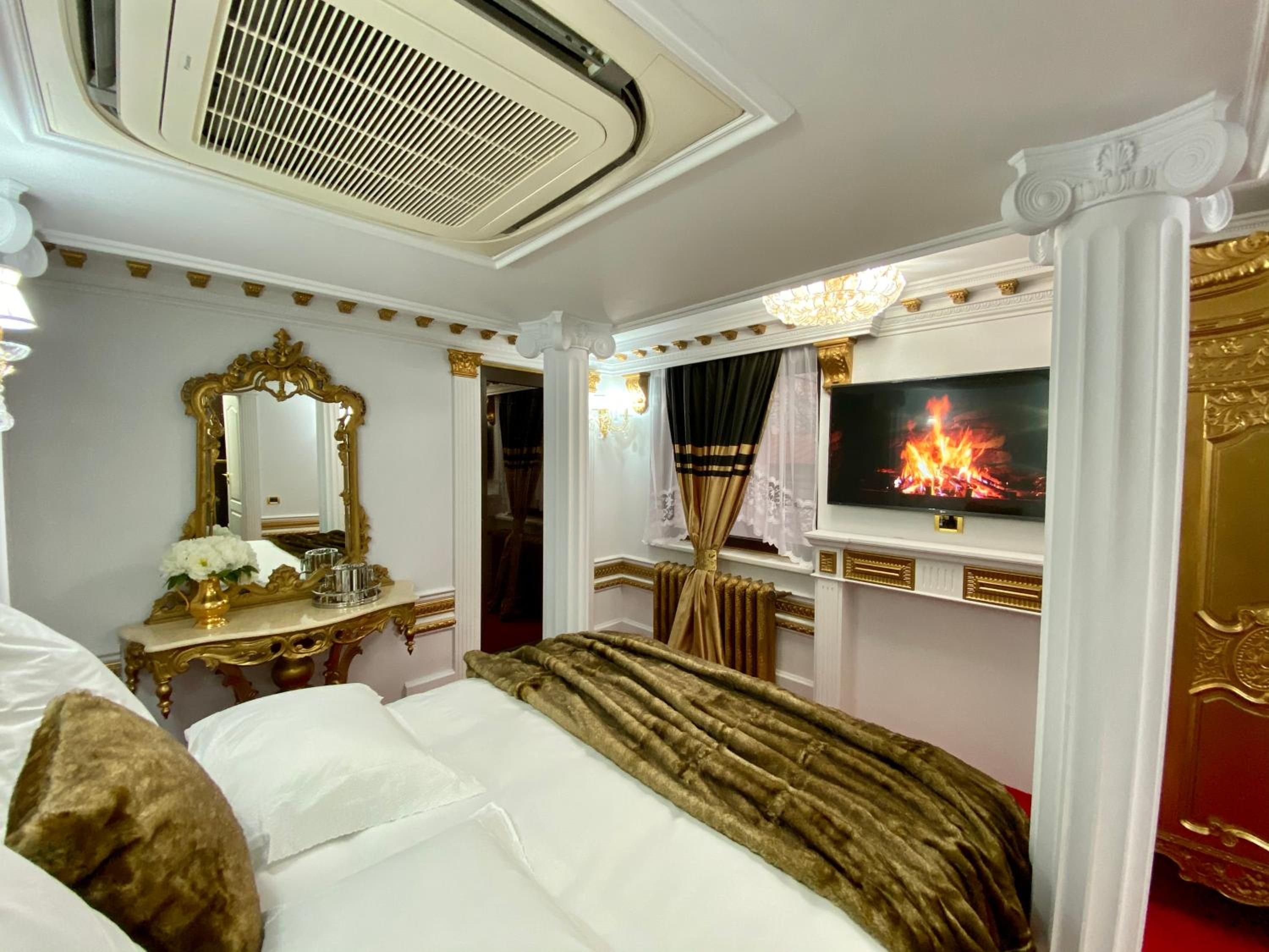Un dormitorio lujoso con una cama grande, un televisor mostrando un fuego y una decoración elaborada.