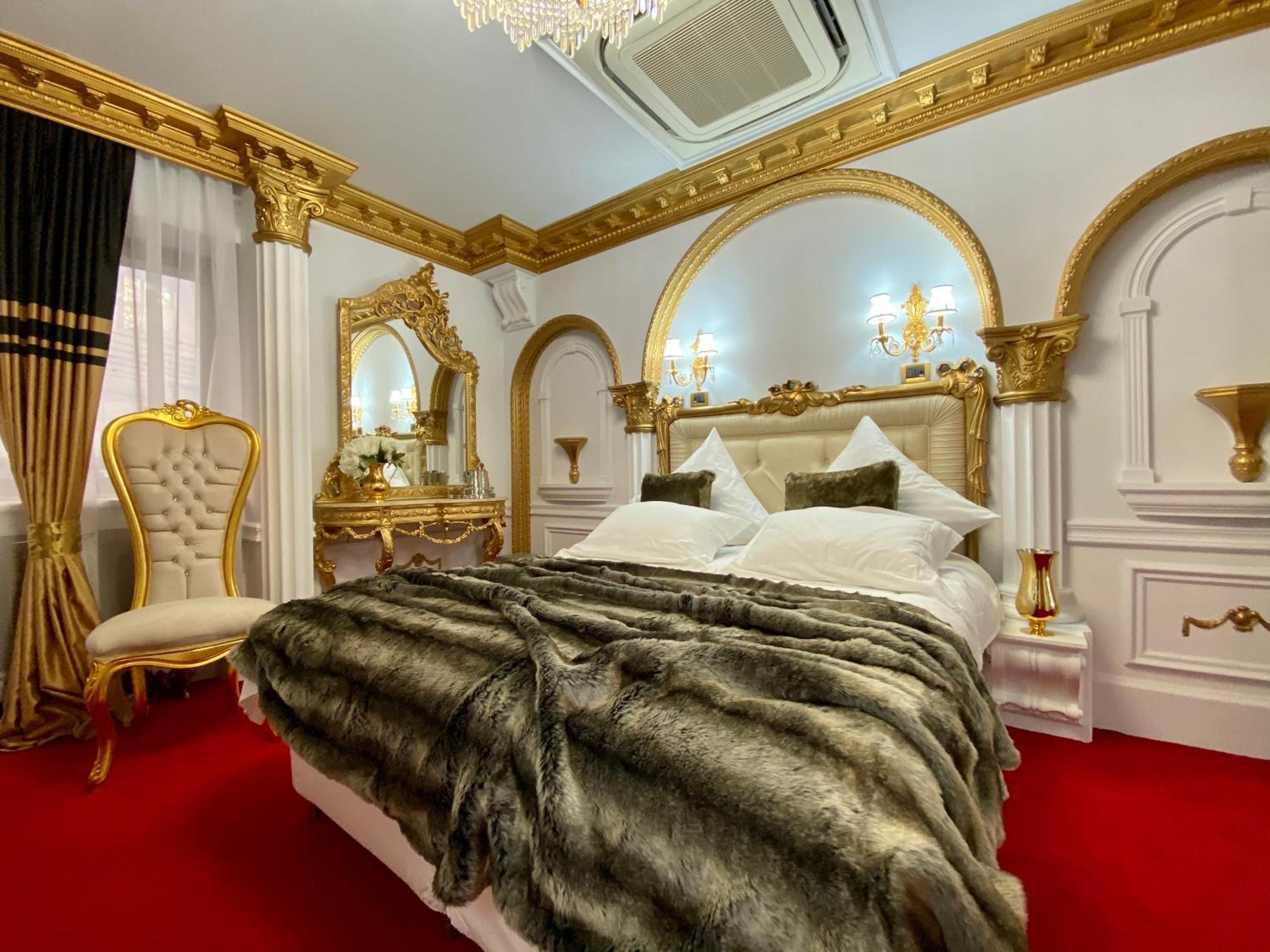 A luxurious bedroom with a large bed, ornate gold detailing, and a red carpet.