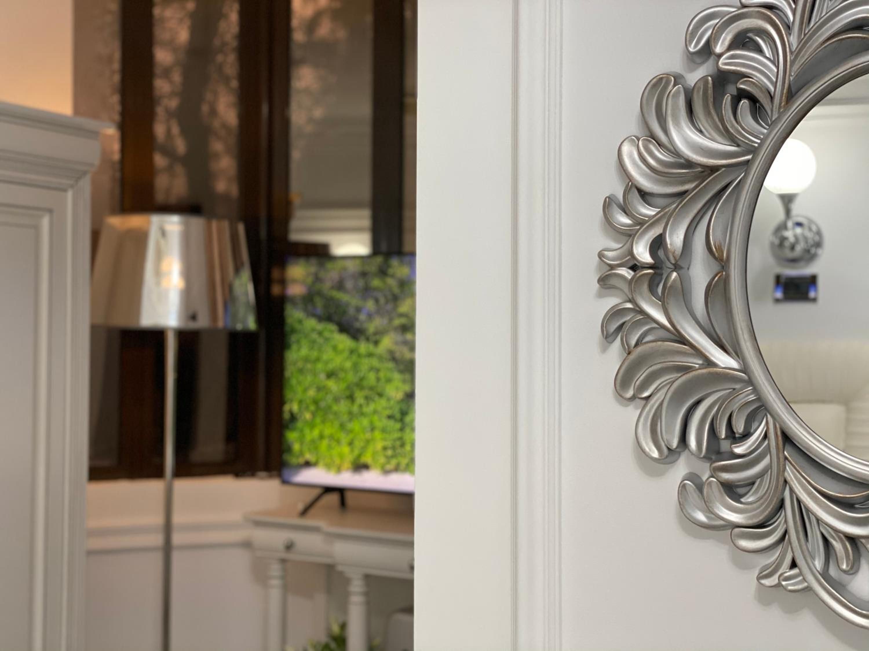 Une pièce avec un téléviseur posé sur un meuble, une lampe et un miroir décoratif accroché au mur.