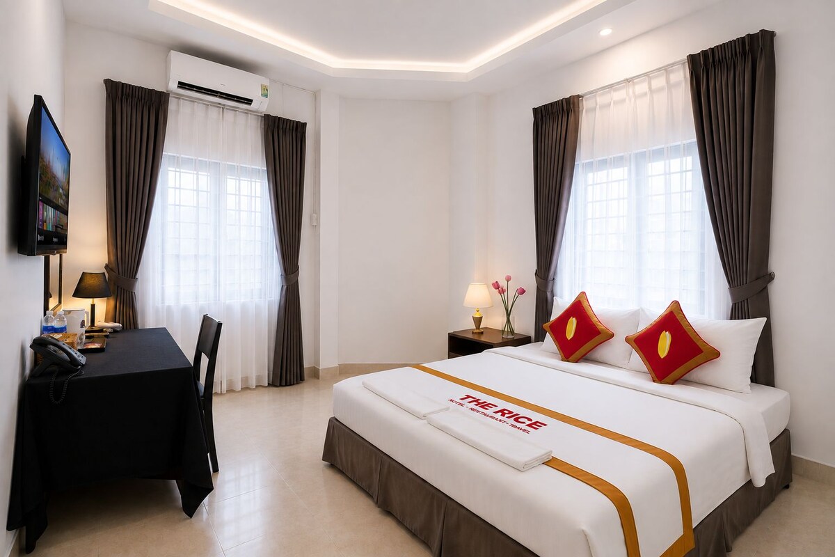 A hotel room with a bed, a desk, a chair, a TV, and an air conditioning unit.