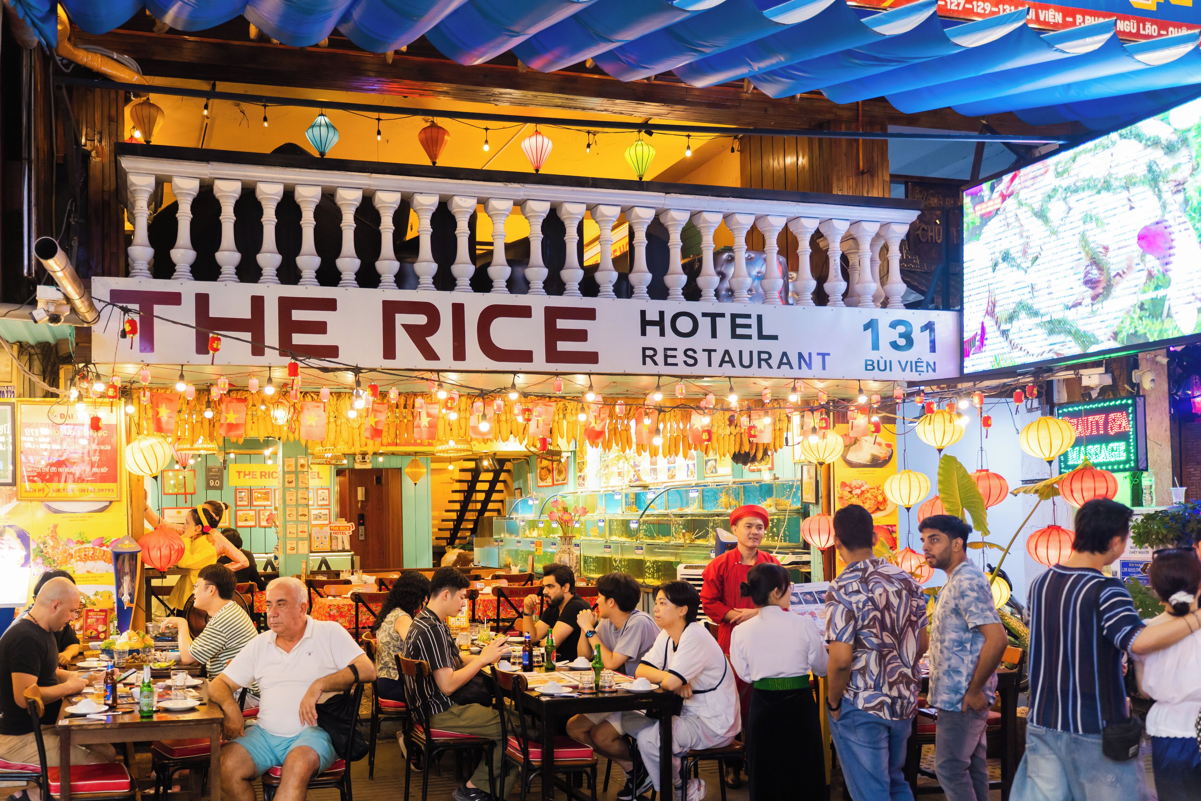 A bustling restaurant with a sign reading 'The Rice Hotel Restaurant 131.'