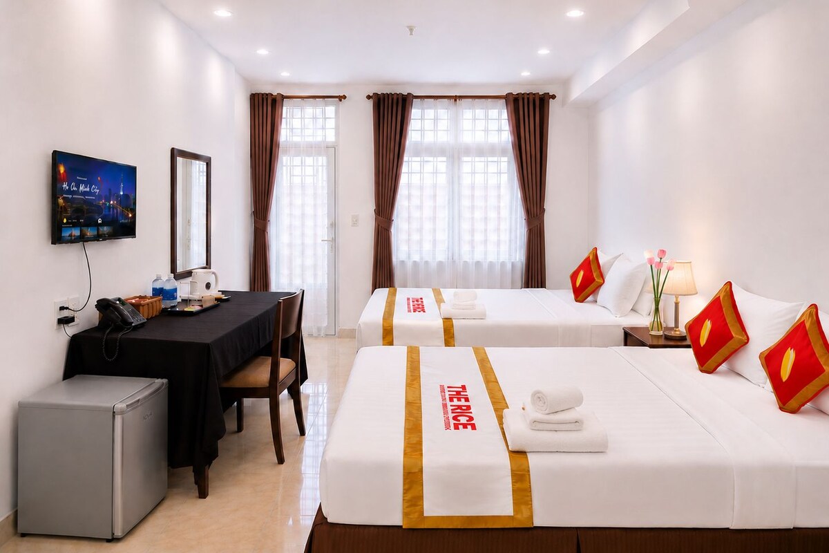 A hotel room with two beds, a desk with a computer, a refrigerator, and a television mounted on the wall.