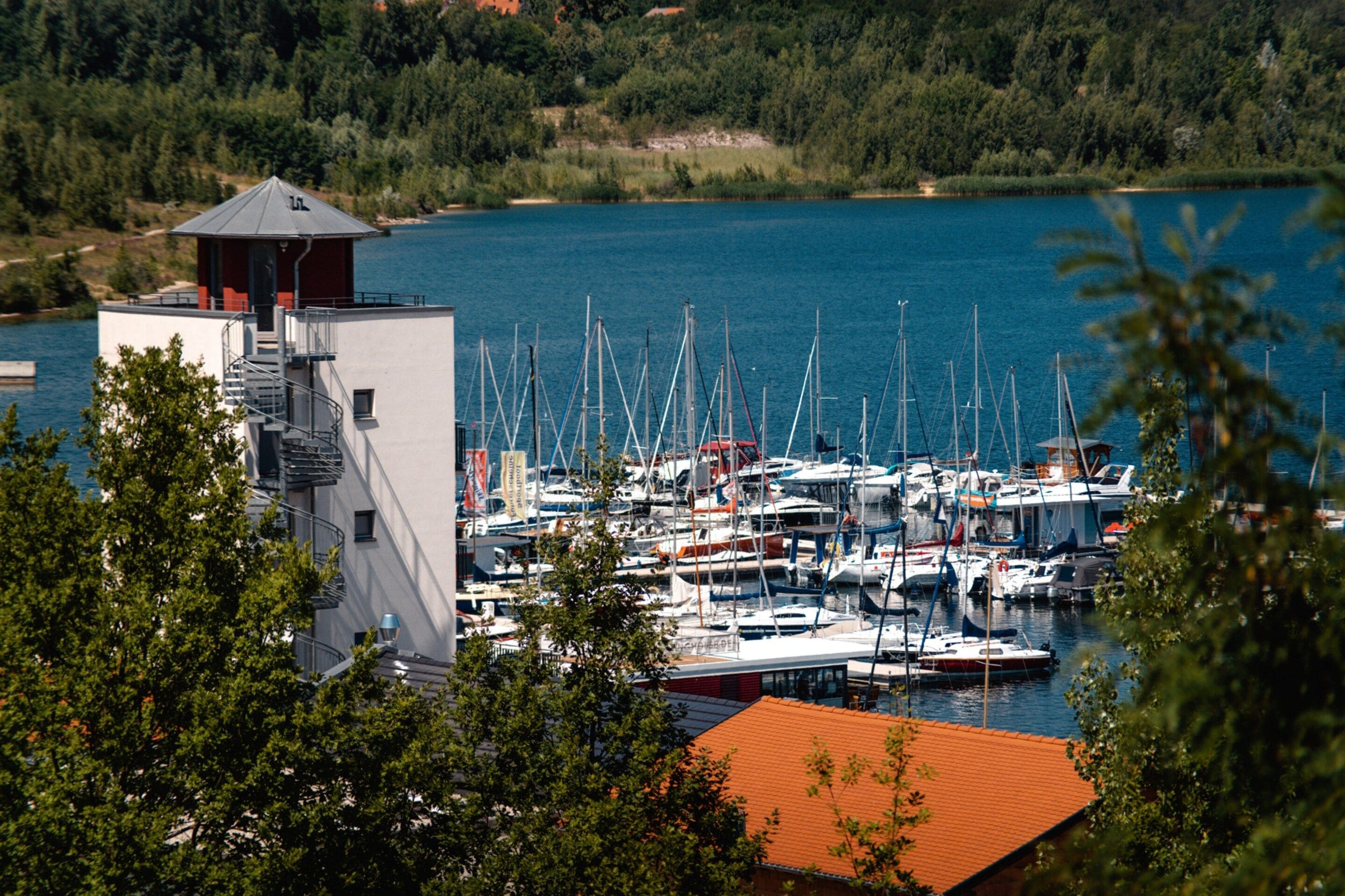 Ein Yachthafen mit mehreren vertäuten Booten, ein Gebäude mit rotem Dach und ein Turm mit rotem Dach.