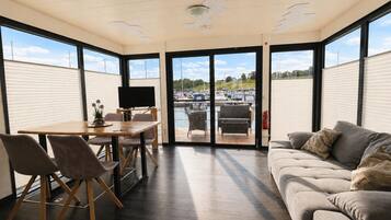 A modern interior with a dining area, a sofa, and a view of a marina through large windows.