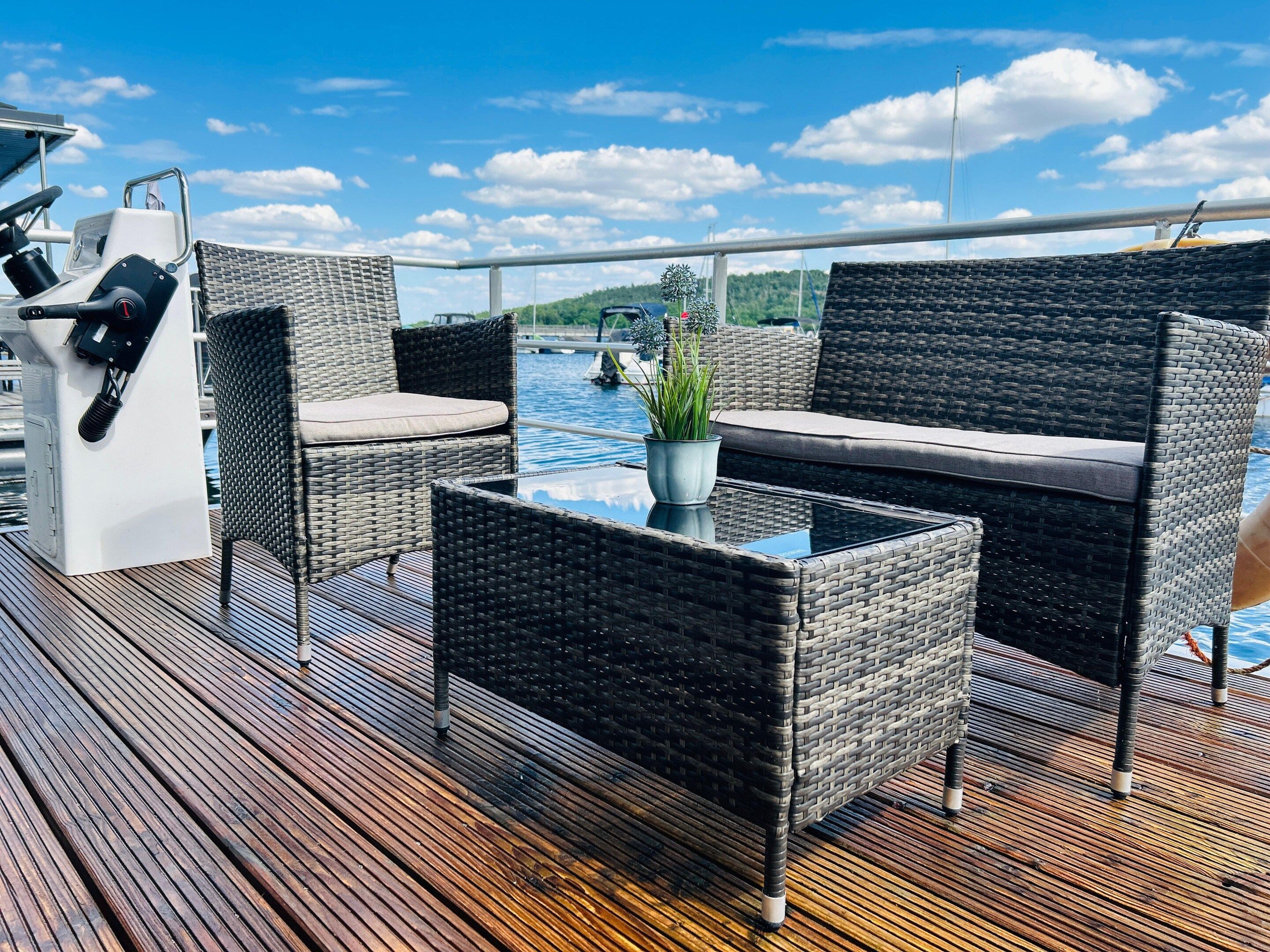 A deck with wicker furniture, a glass table, and a control panel.