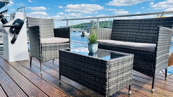 A deck with wicker furniture, a glass table, and a control panel.