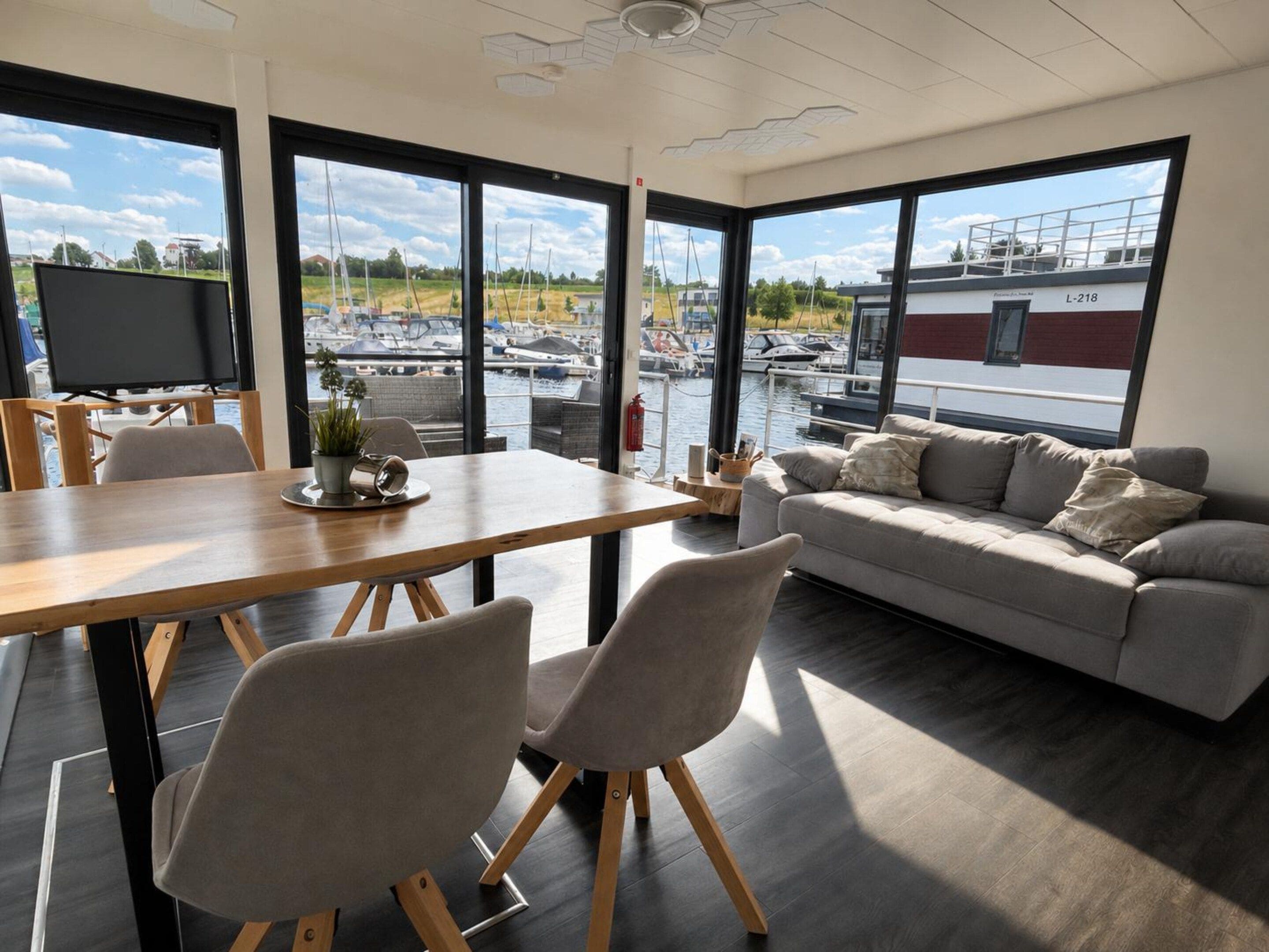 A modern interior with a dining area, sofa, and large windows overlooking a marina.