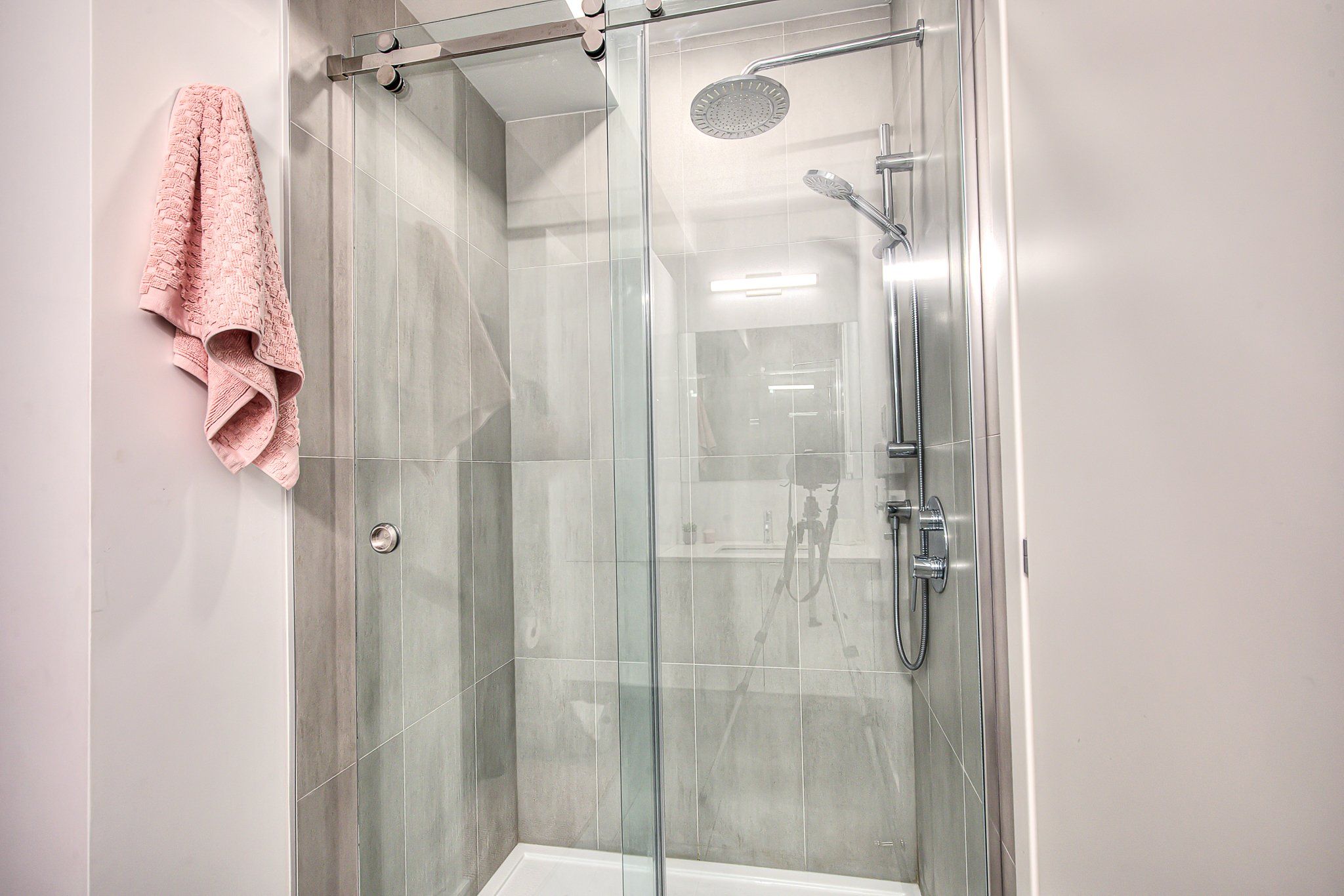 A glass-enclosed shower with a handheld showerhead and a wall-mounted faucet.