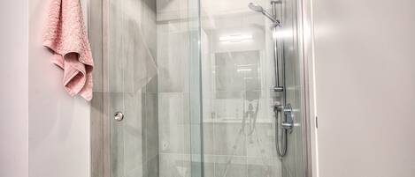 A glass-enclosed shower with a handheld showerhead and a wall-mounted faucet.