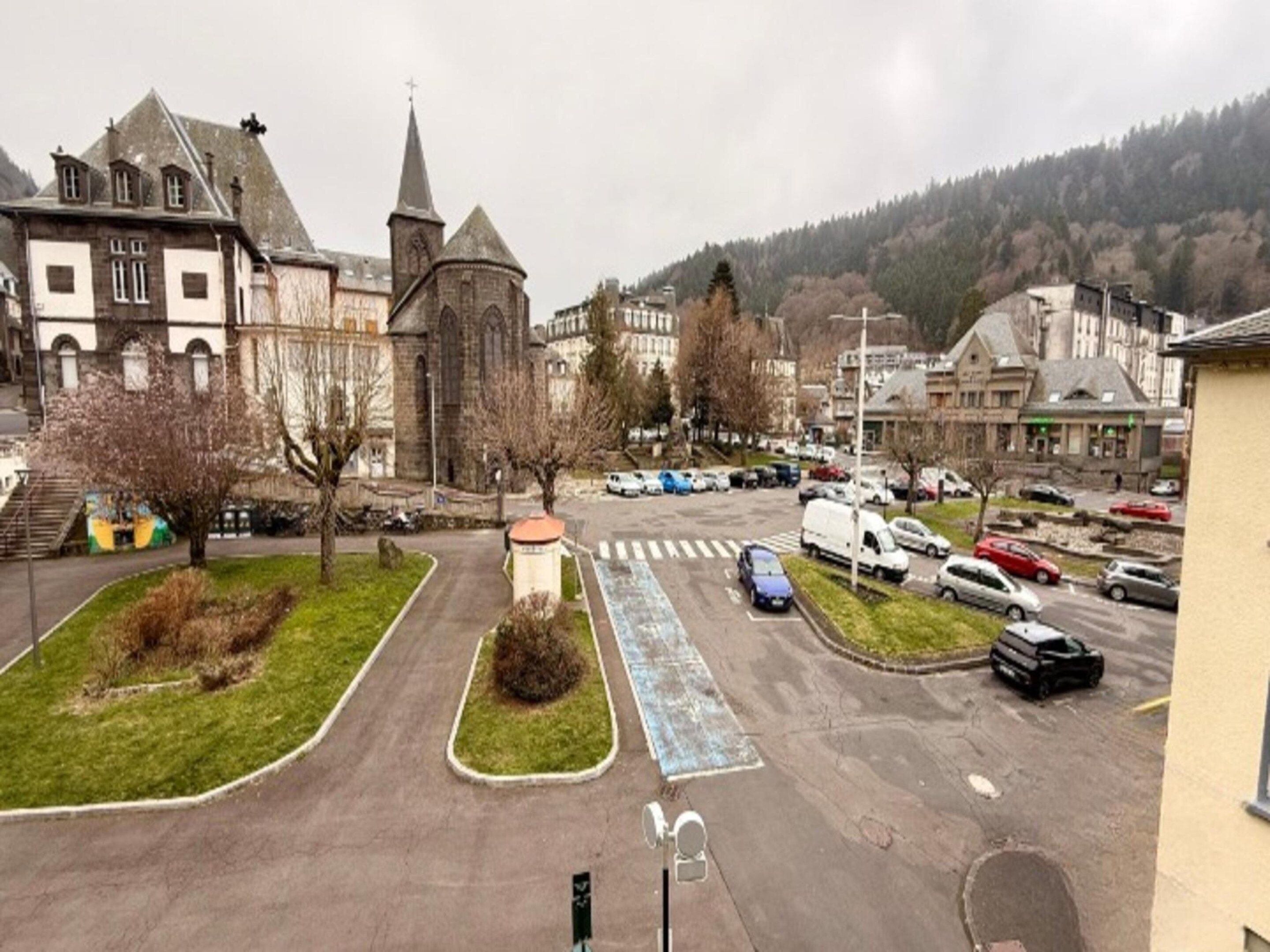 Un parking rempli de voitures, une église avec un clocher imposant et des immeubles d’habitation en arrière-plan.
