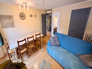 Ein Wohnzimmer mit blauem Sofa, Esstisch aus Holz und Stühlen. An der Wand hängt eine Uhr, und es gibt eine Stern-Dekoration.