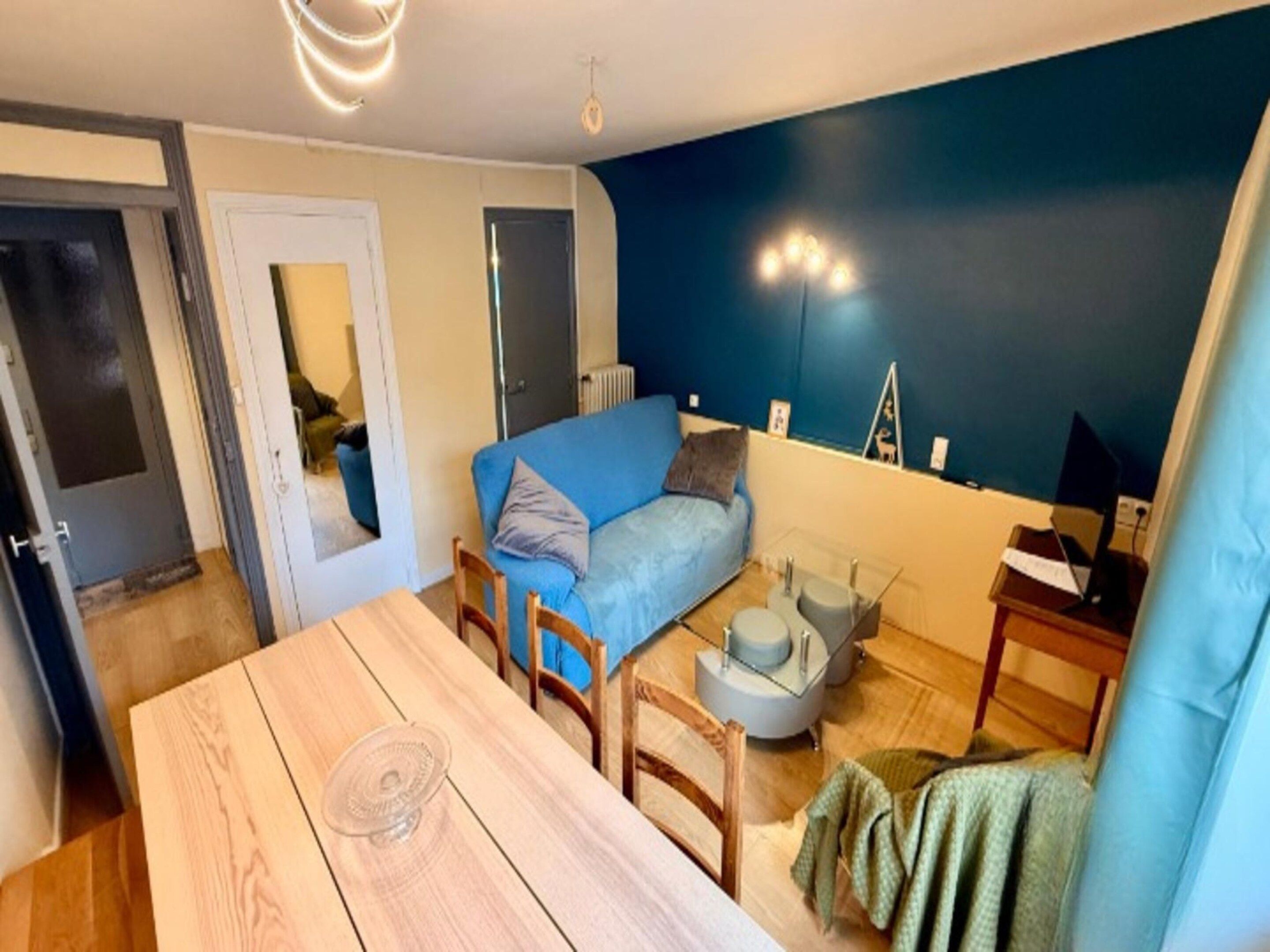 A compact living space with a dining table, a blue sofa, and a small kitchenette area.